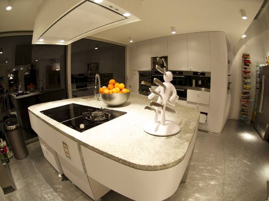 Una cocina moderna con una isla central, un fregadero y una estufa. Hay un bol con naranjas sobre la isla y una escultura blanca.