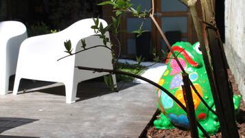 Un jardin avec une chaise blanche, une sculpture de grenouille verte et une clôture en bois.