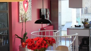 Una cocina moderna con pared rosa, barandilla blanca y lámpara colgante negra.