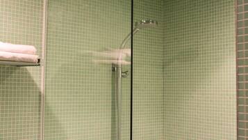 A bathroom with green tiled walls, a glass shower enclosure, and a towel rack with a white towel.