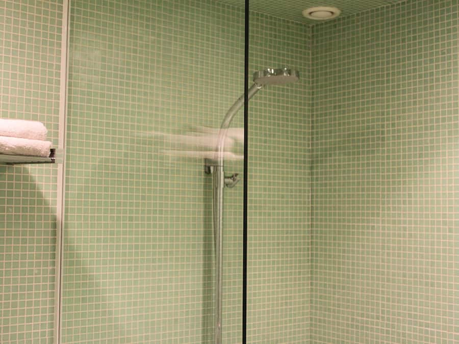 A bathroom with green tiled walls, a glass shower enclosure, and a towel rack with a white towel.