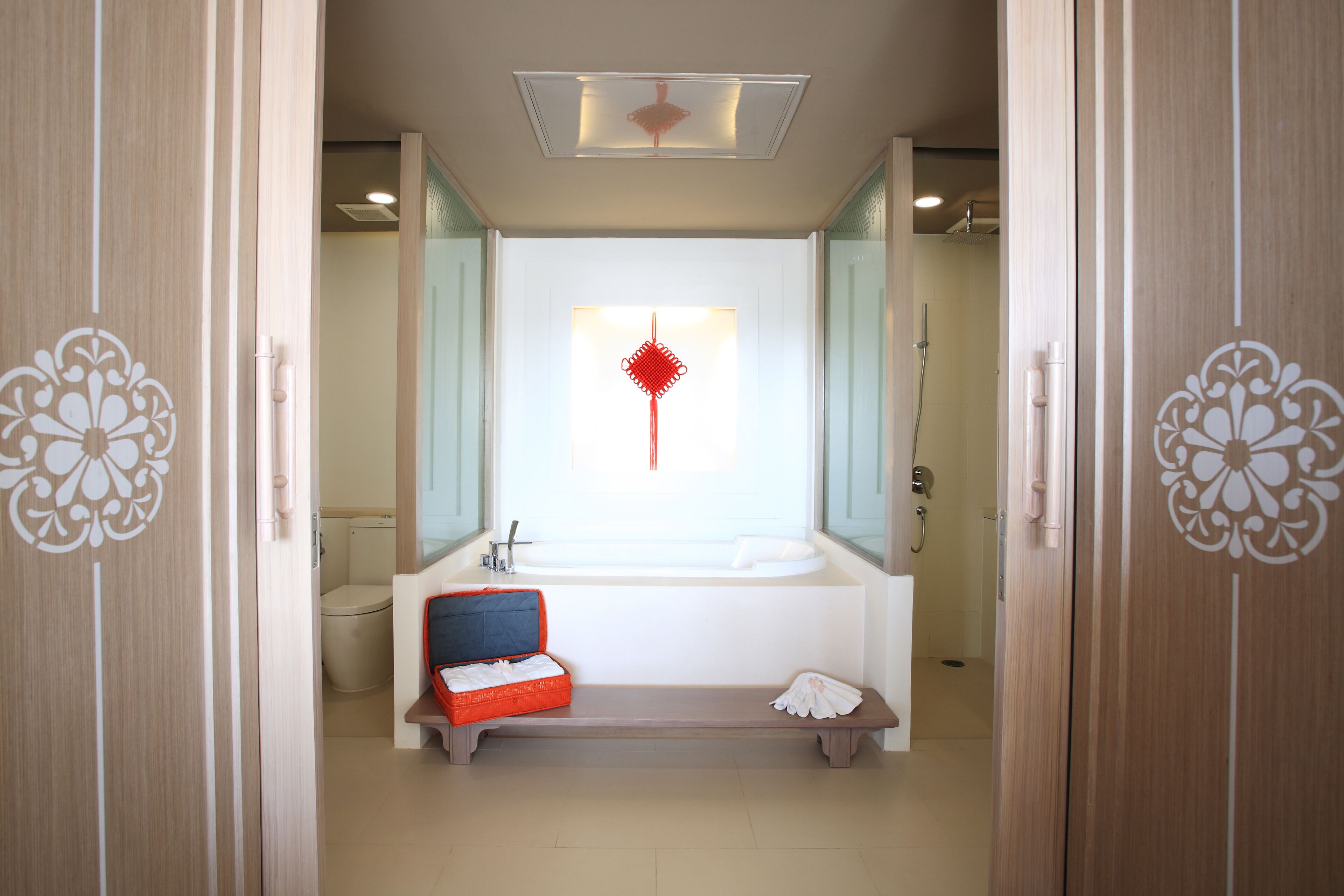 Un baño con un espejo grande, un lavabo blanco, un neceser rojo y un banco.