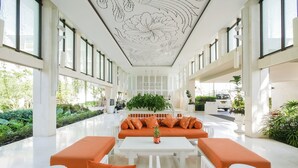 Un vestíbulo amplio con una zona de estar central, cojines naranjas, mobiliario blanco y un techo decorativo.