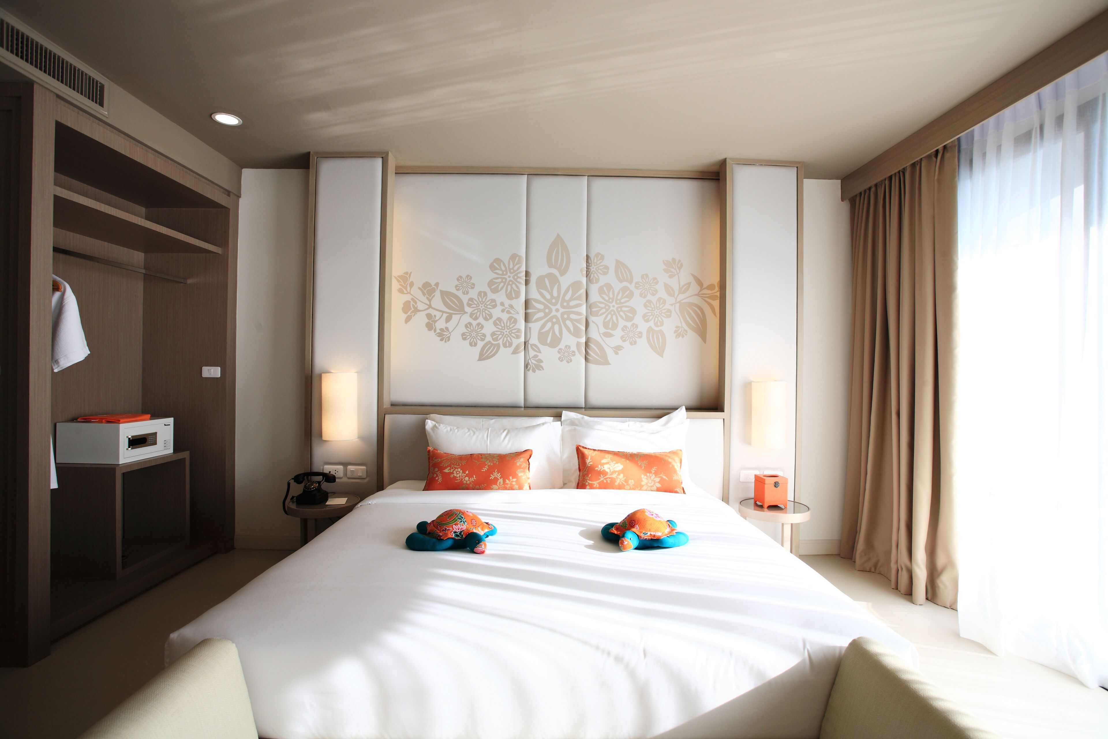 Habitación de hotel con una cama grande, dos almohadas, una mesita de noche con lámpara, un armario y vistas al exterior.