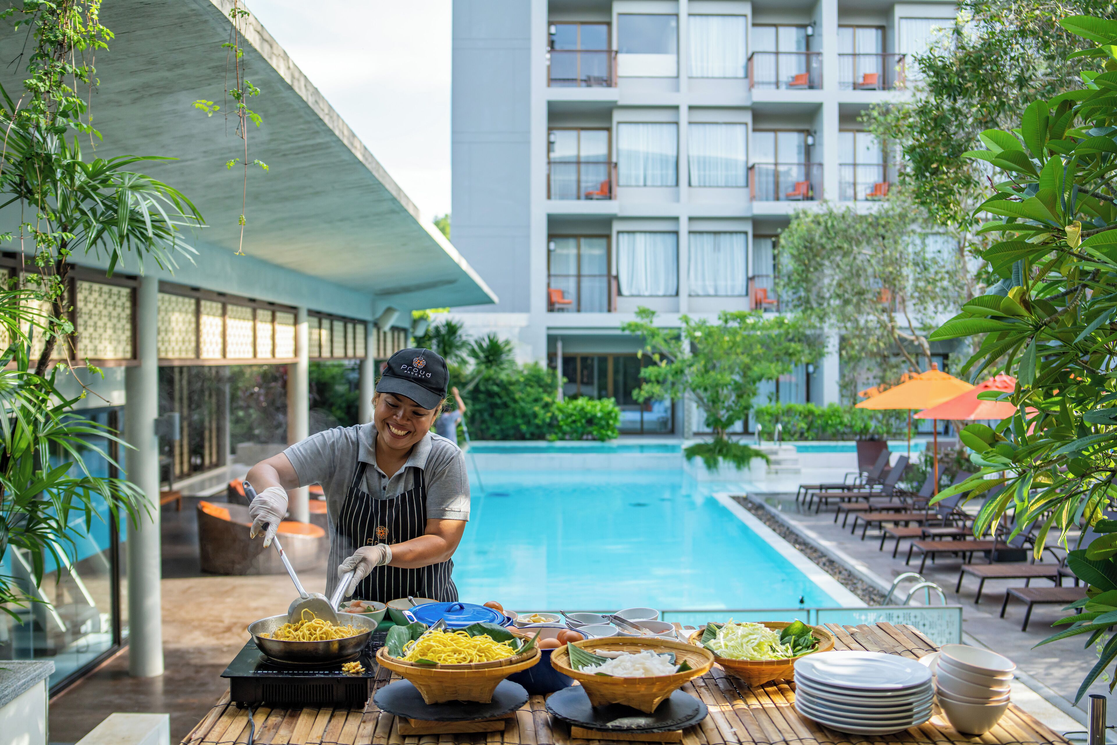 Un espace de restauration situé au bord de la piscine, avec un chef qui prépare les plats, une piscine et des chaises longues.