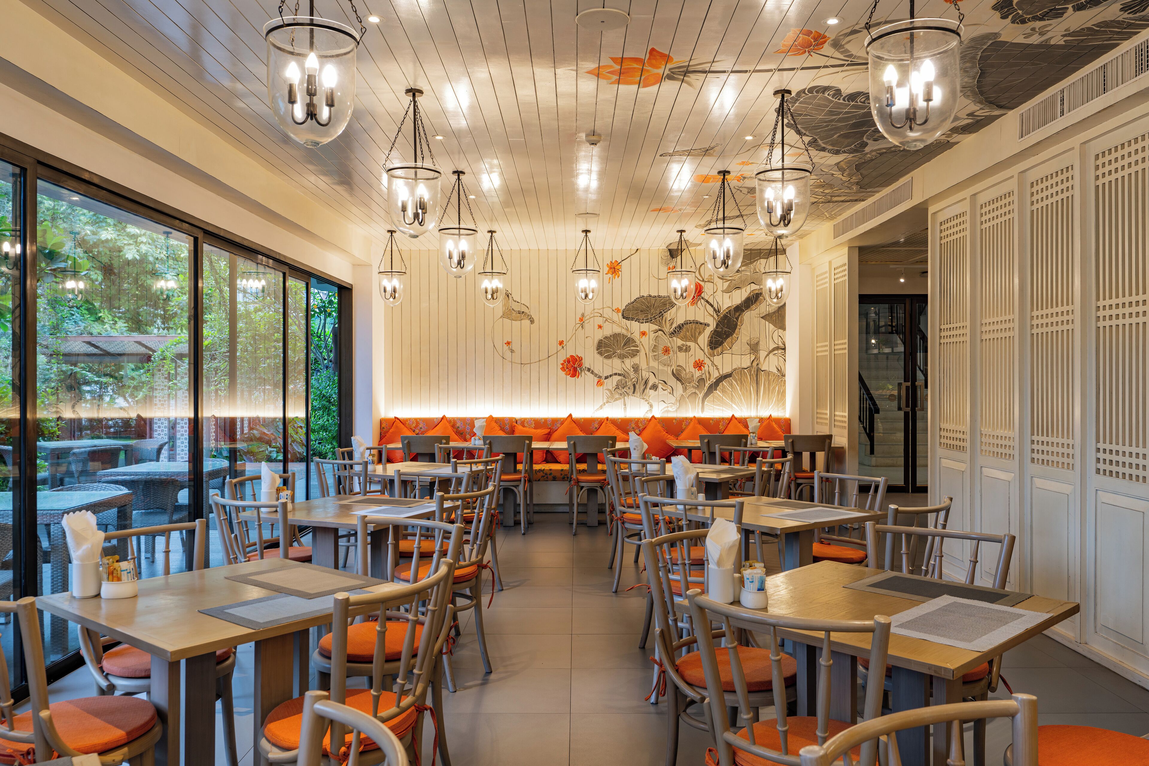 A restaurant interior with multiple tables and chairs, large windows, and hanging pendant lights.