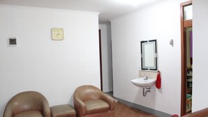 A room with two leather armchairs, a white sink with a mirror, and a clock on the wall. - De Sun Pasteur Guest House by HouseinBandung (Bandung)