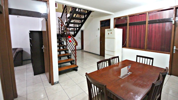 A dining area with a wooden table and chairs, a staircase, and a refrigerator. - De Sun Pasteur Guest House by HouseinBandung (Bandung)
