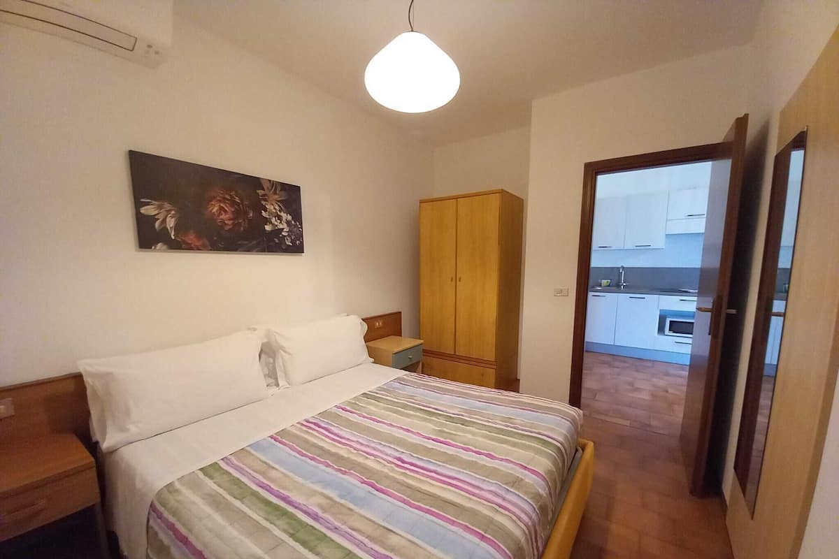 A bedroom with a bed, a wooden wardrobe, a nightstand, and a painting on the wall.