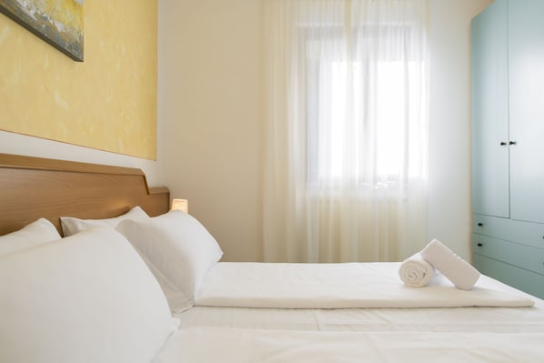 A neatly made bed with white linens, a rolled towel, and a wooden headboard.