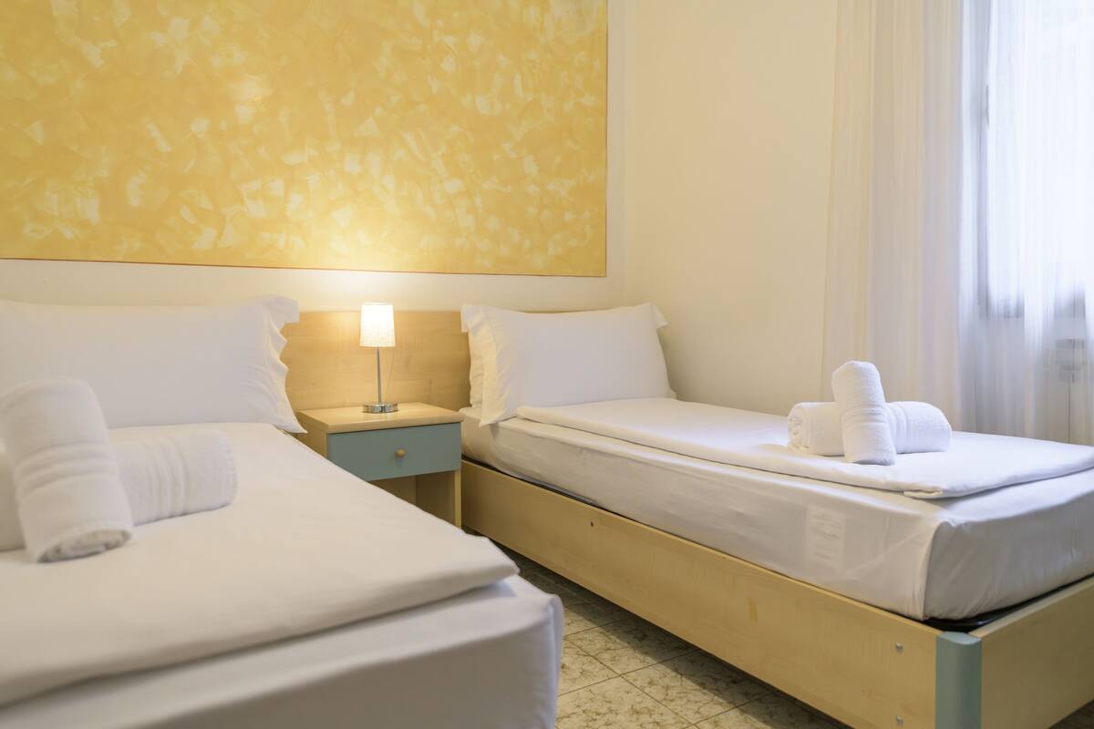 A hotel room with two beds, a nightstand with a lamp, and a large abstract painting on the wall.