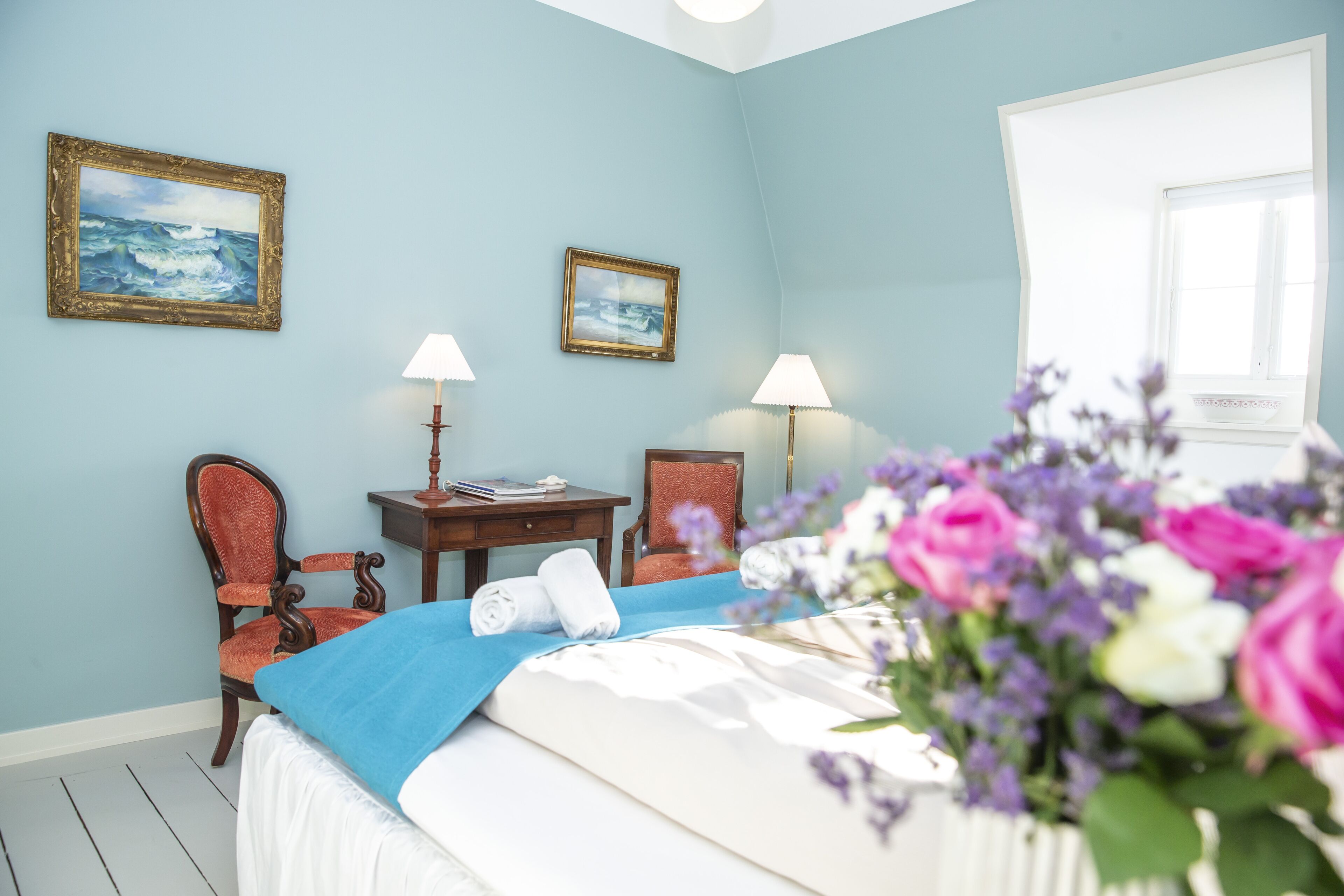 A bedroom with a bed, two chairs, a desk, and two lamps.