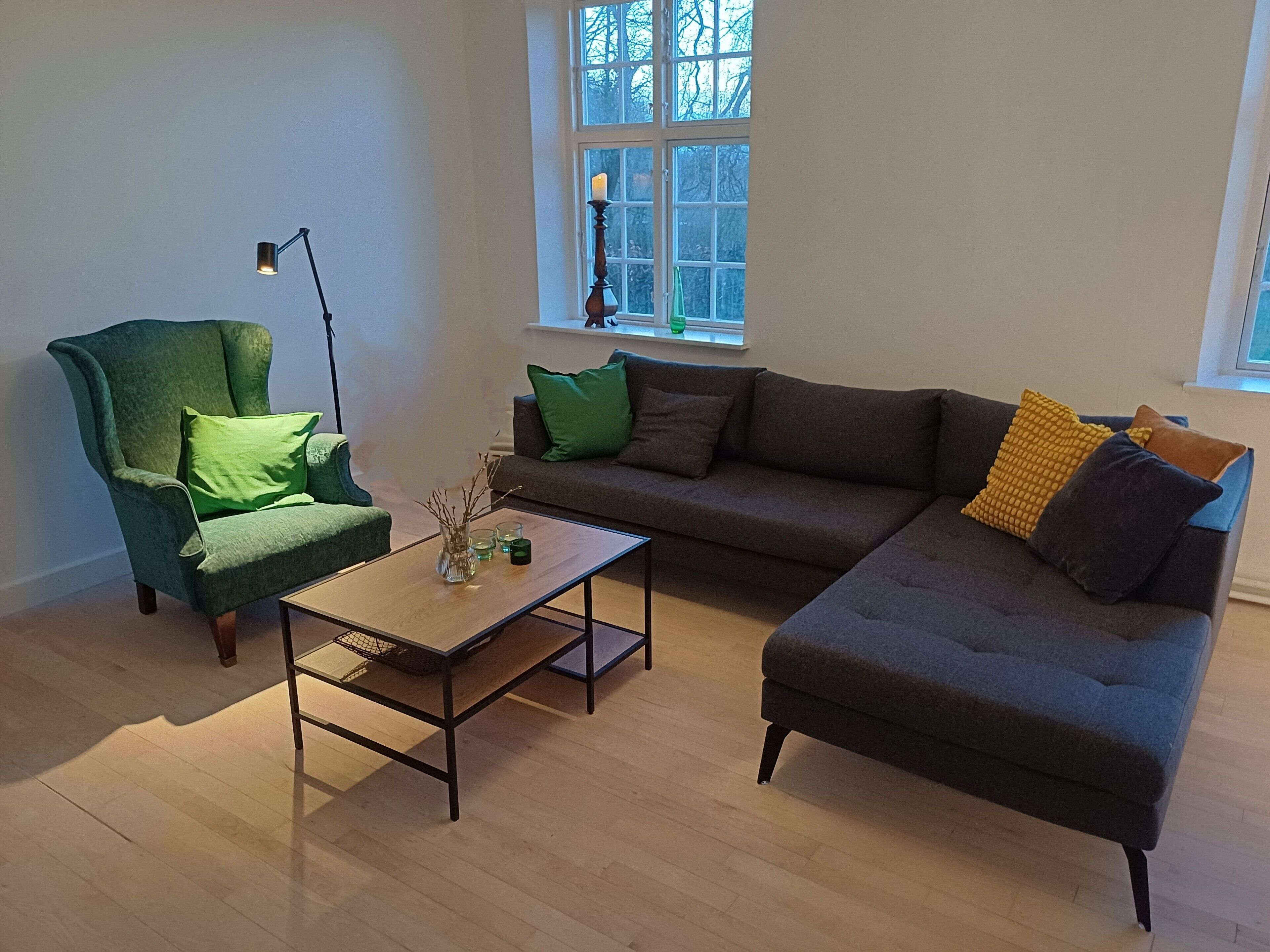 A living room with a green armchair, a grey sofa, a wooden coffee table, and a floor lamp.