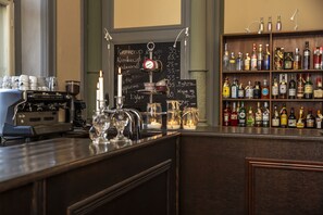 A bar area with a coffee machine, a chalkboard menu, and a shelf of liquor bottles.