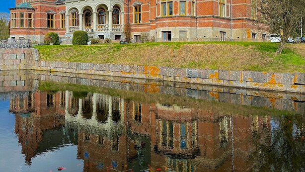 A large, historic brick building with arched windows and a reflection in the water in front. - Fuglsang Herregaard Hotel (Toreby)