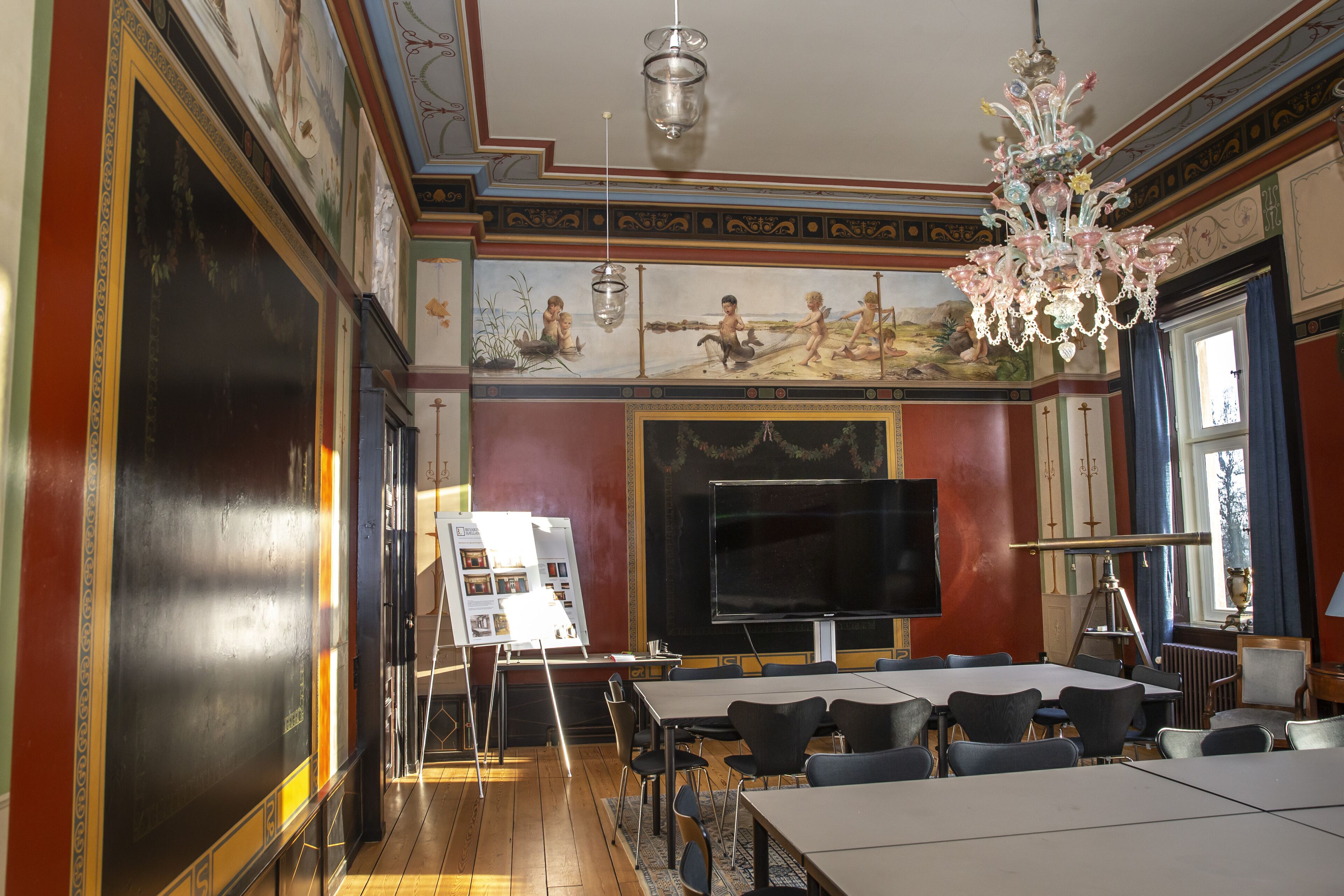 A classroom with a large blackboard, whiteboard, and a projector screen. There are desks and chairs arranged for seating.