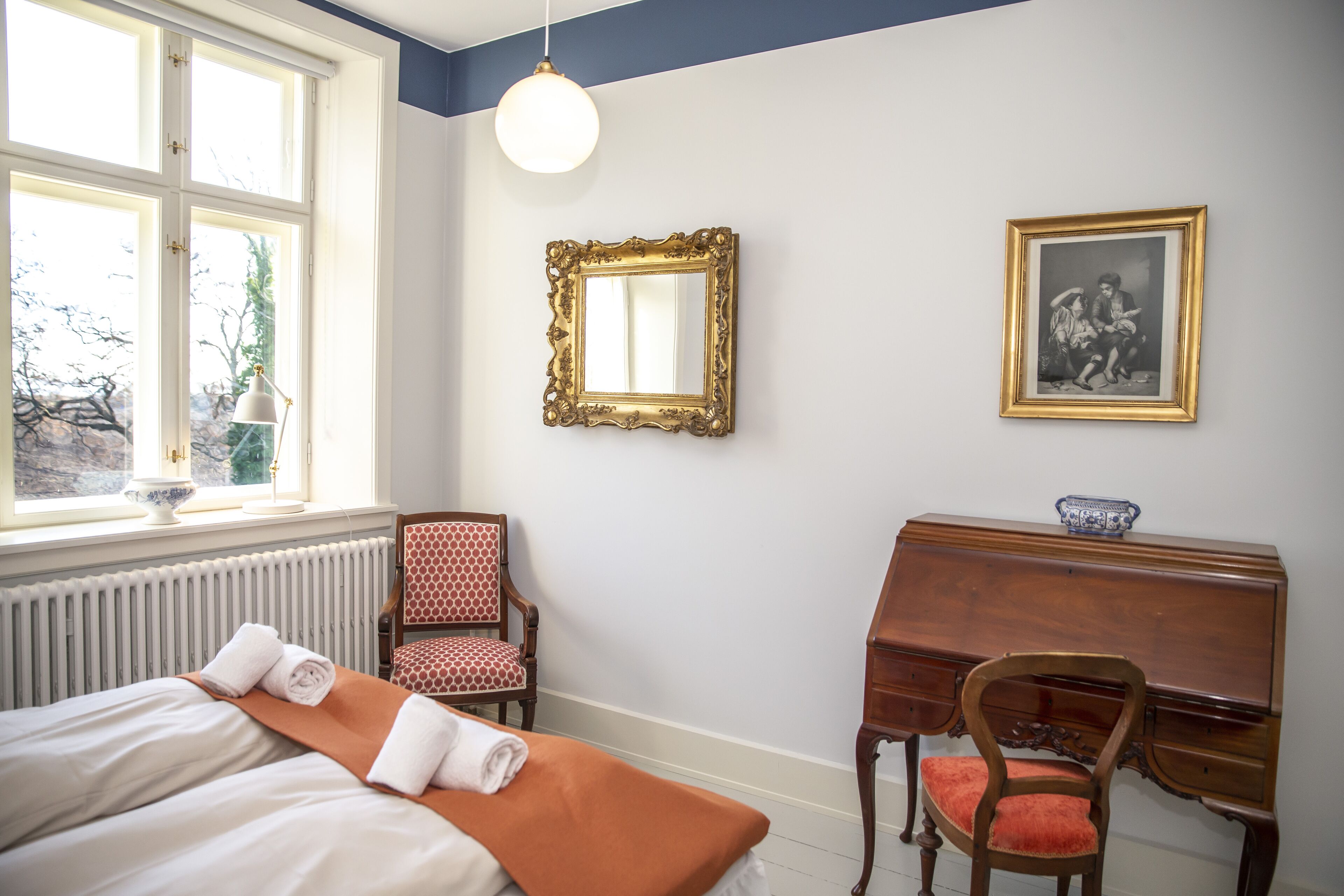 Habitación de hotel con cama, escritorio, silla, espejo y ventana con vista a árboles.