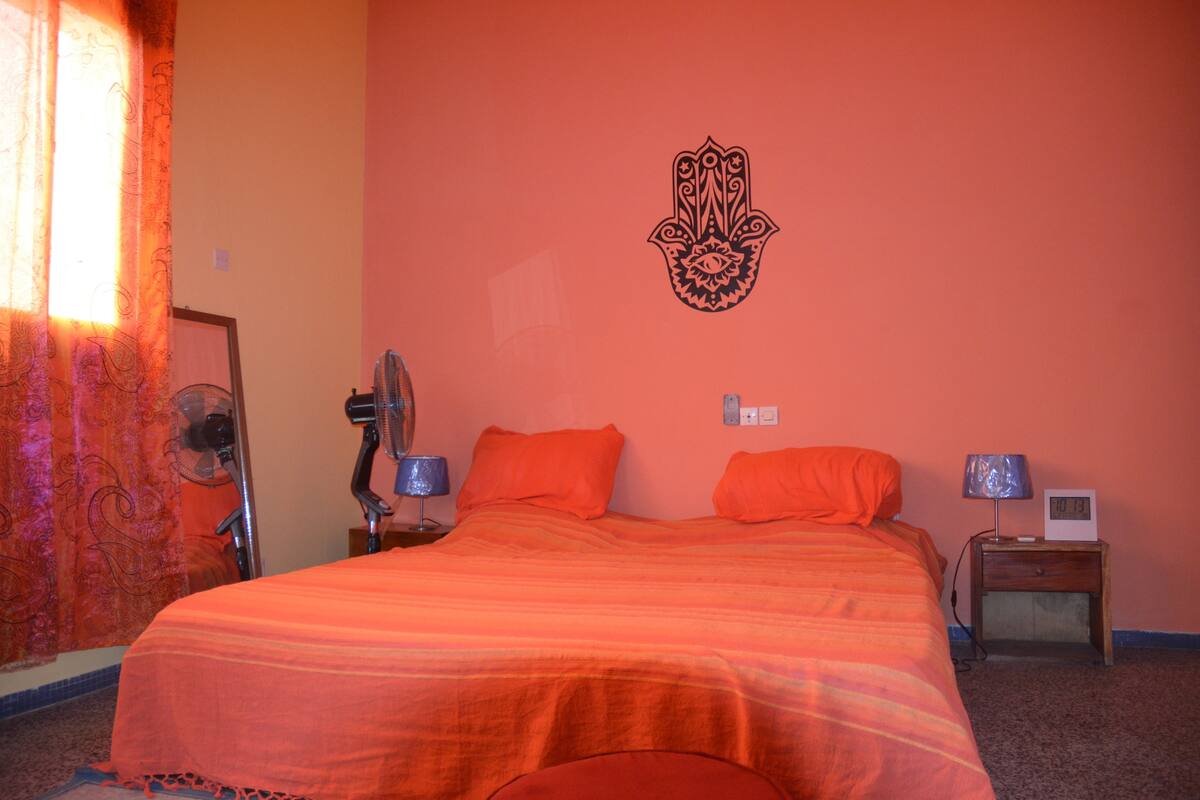 A room with a bed, two nightstands, a wall clock, and a decorative wall hanging.