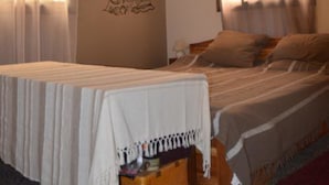 A bedroom with a bed, a nightstand, and a wall decoration. - Hotel Restaurant Coté Sud (Lomé)
