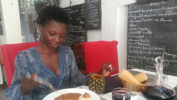 A person dining at a restaurant with a menu on the wall, a plate of food, a glass of red wine, and a bottle of water. - Hotel Restaurant Coté Sud (Lomé)