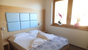 Een slaapkamer met een houten hoofdeinde, een bed met witte lakens, een nachtkastje en een raam met uitzicht.