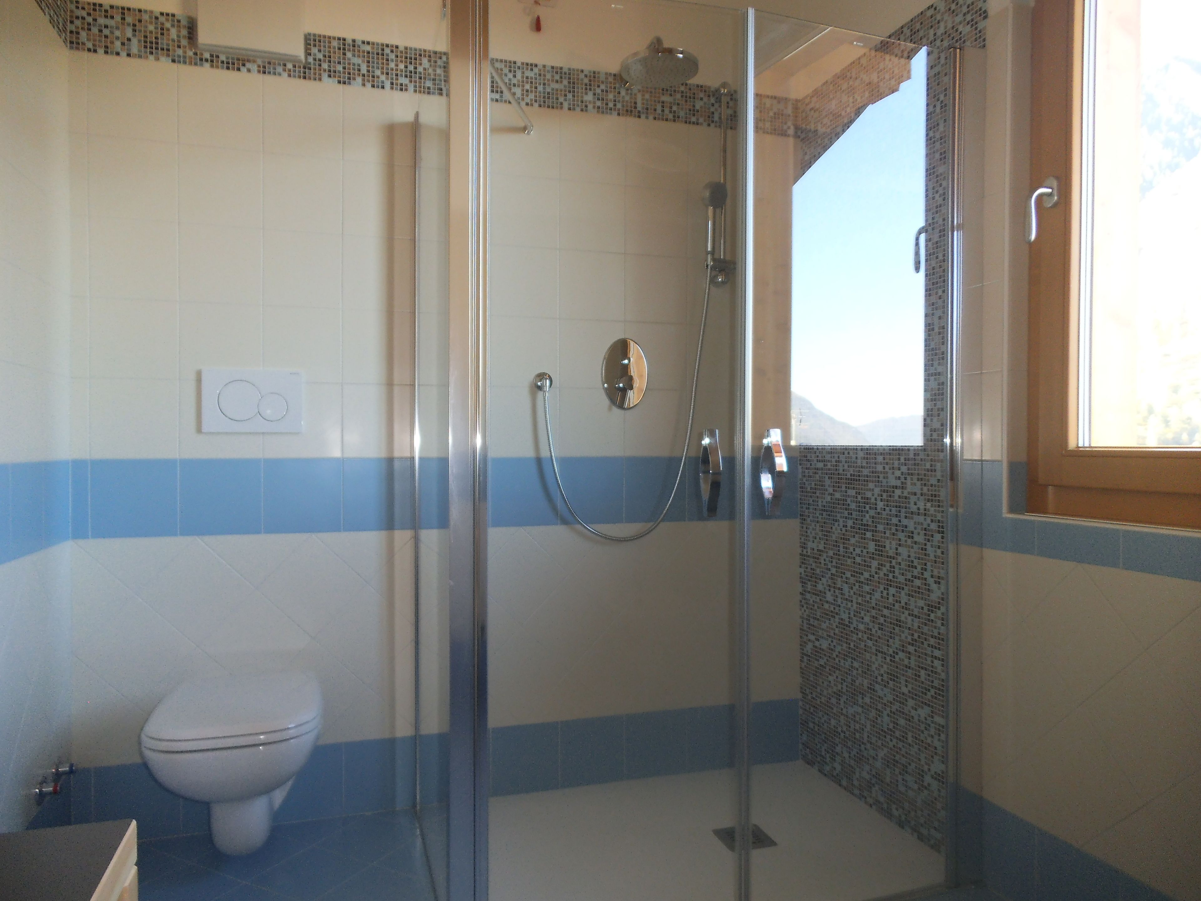 A bathroom with a glass-enclosed shower, a toilet, and a window providing natural light.