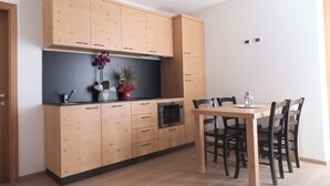 Een moderne keuken met houten kastjes, een zwart aanrecht en een eettafel met stoelen.