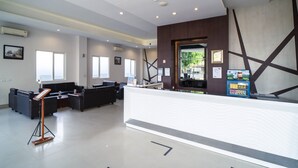 A modern reception area with a reception desk, seating area, and a large window offering a view of the outdoors. - Midtown Xpress Sampit Kalimantan Tengah (Sampit)