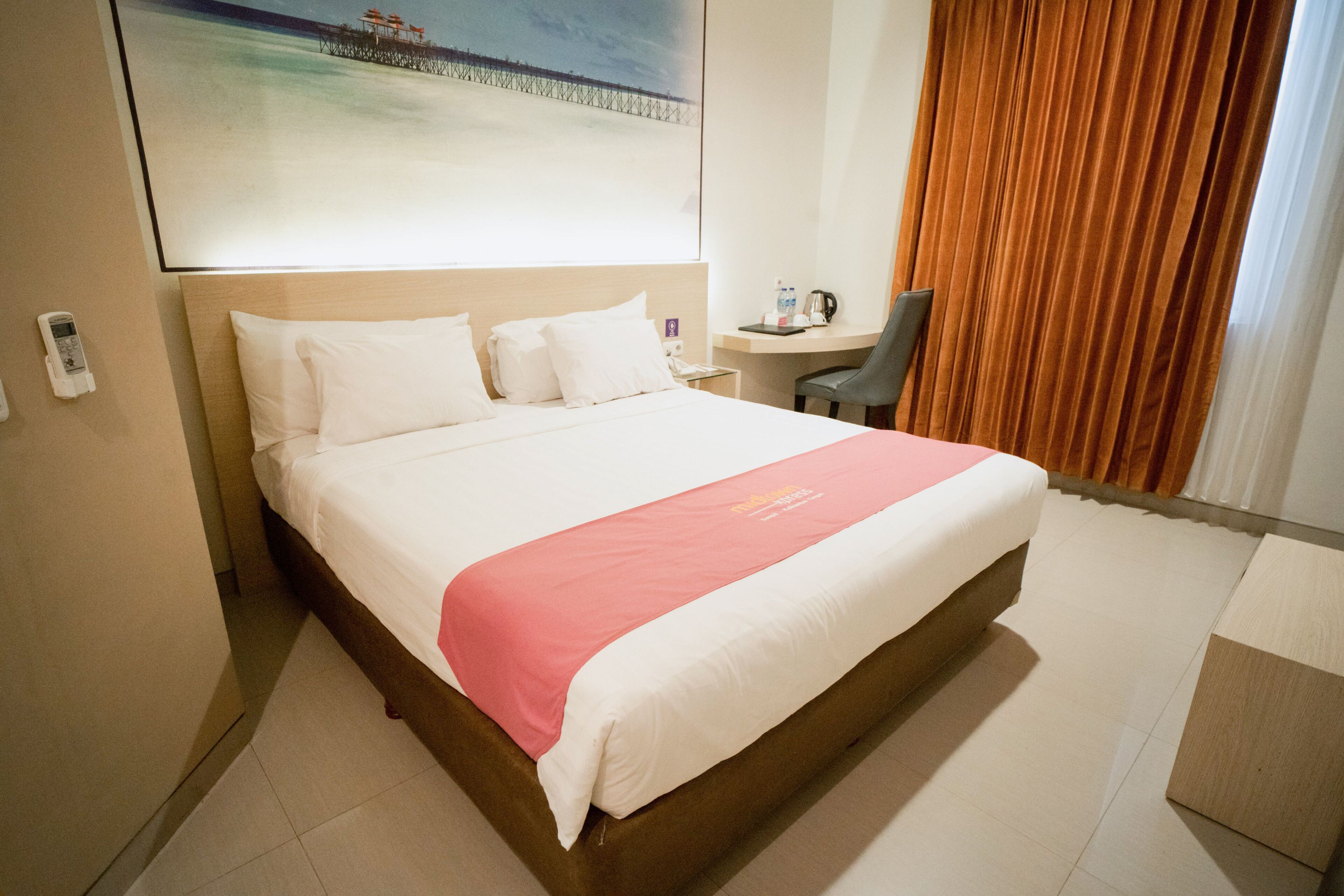 A hotel room with a large bed, a desk, a chair, a phone, and a painting on the wall.