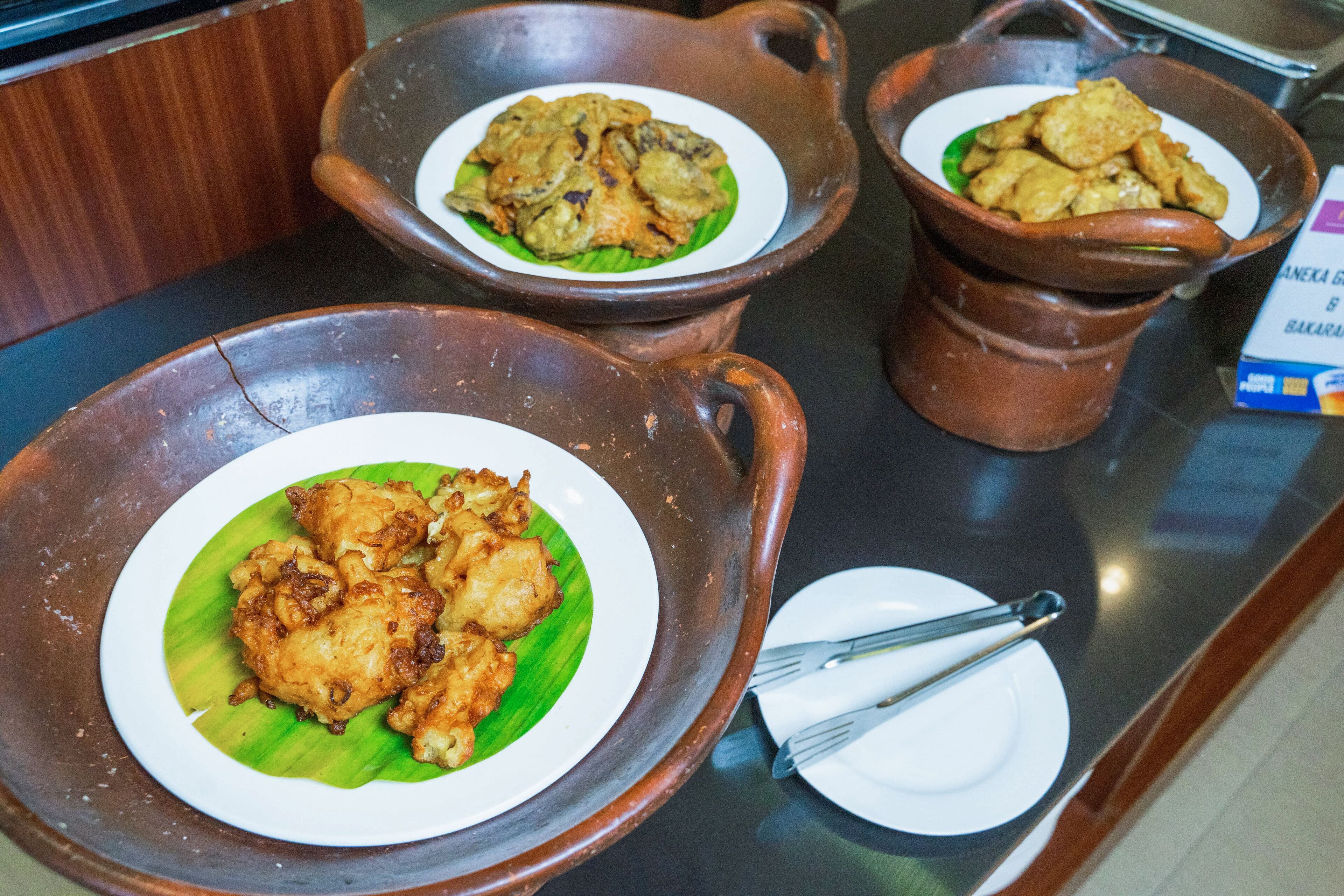 Três vasos de barro com comida frita em uma bancada.