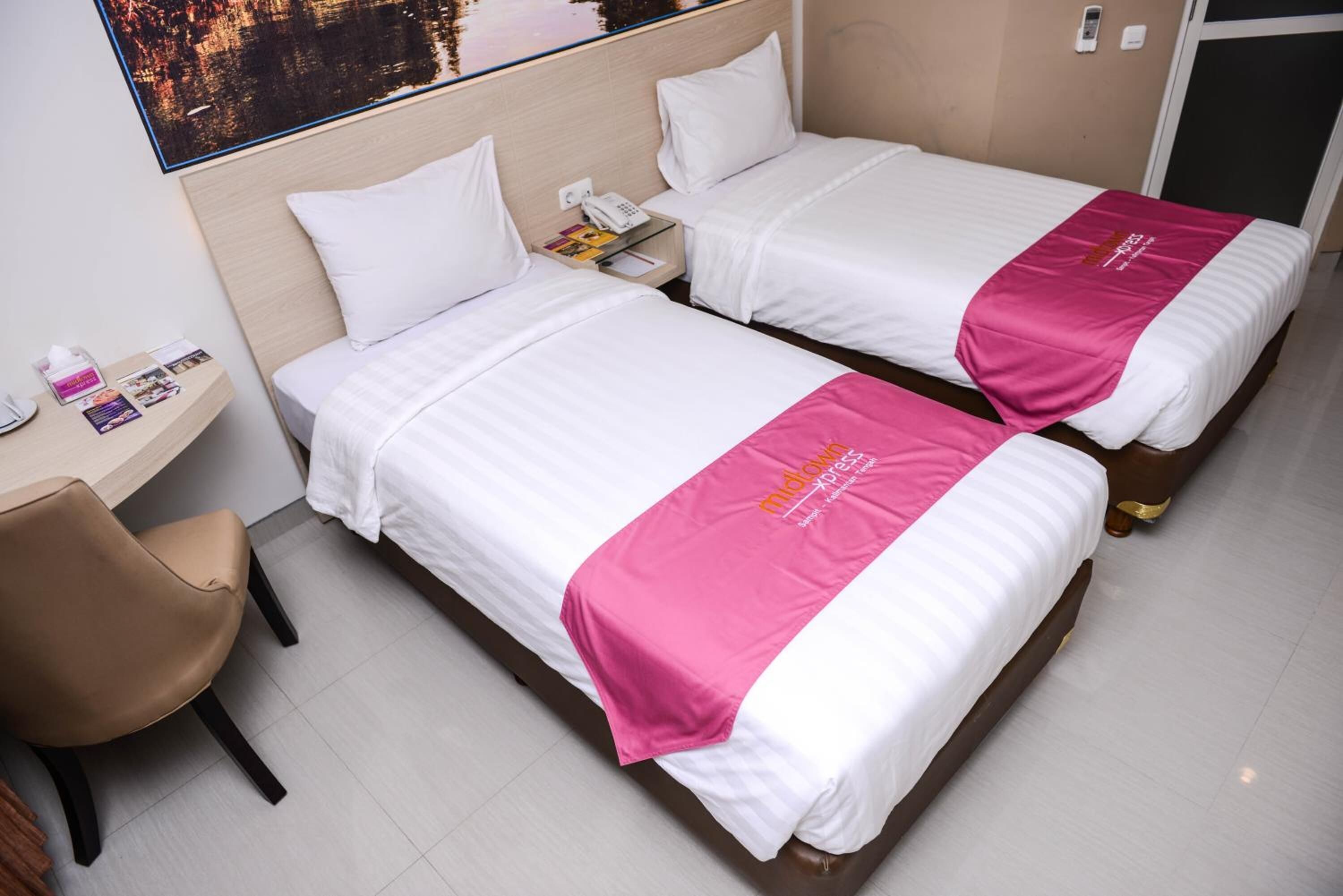 A hotel room with two beds, a desk with a chair, and a nightstand with a phone.