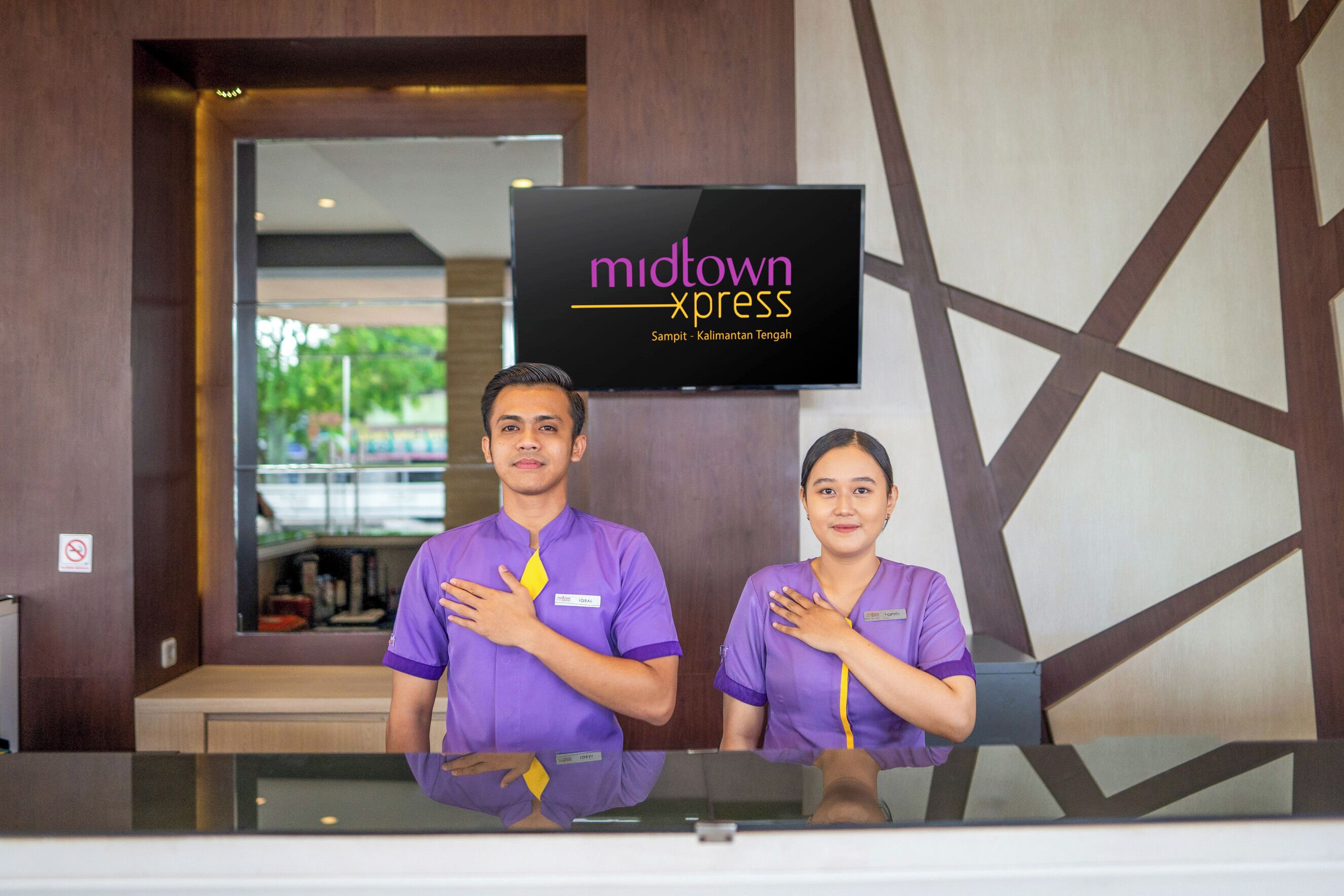 Two receptionists in purple uniforms standing behind a reception desk with a 'midtown xpress' sign above them.