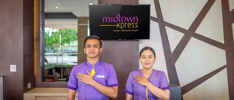 Two receptionists in purple uniforms standing behind a reception desk with a 'midtown xpress' sign above them.