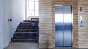 A modern elevator with a metallic finish, a staircase with dark steps, and a wall with a wood-like pattern. - Midtown Xpress Sampit Kalimantan Tengah (Sampit)