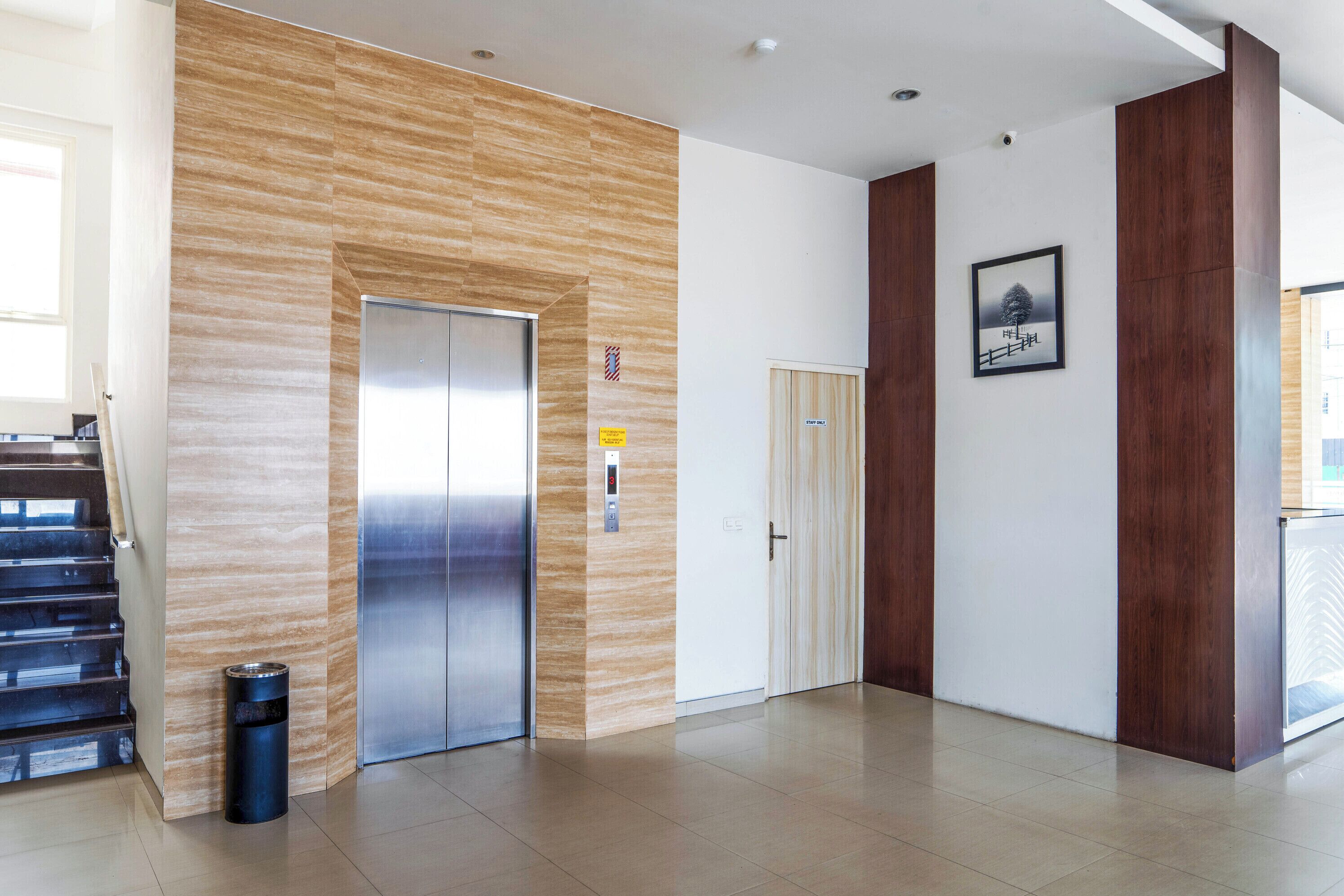 A modern interior with a wooden panel wall, a stainless steel elevator, a trash bin, and a door with a sign.