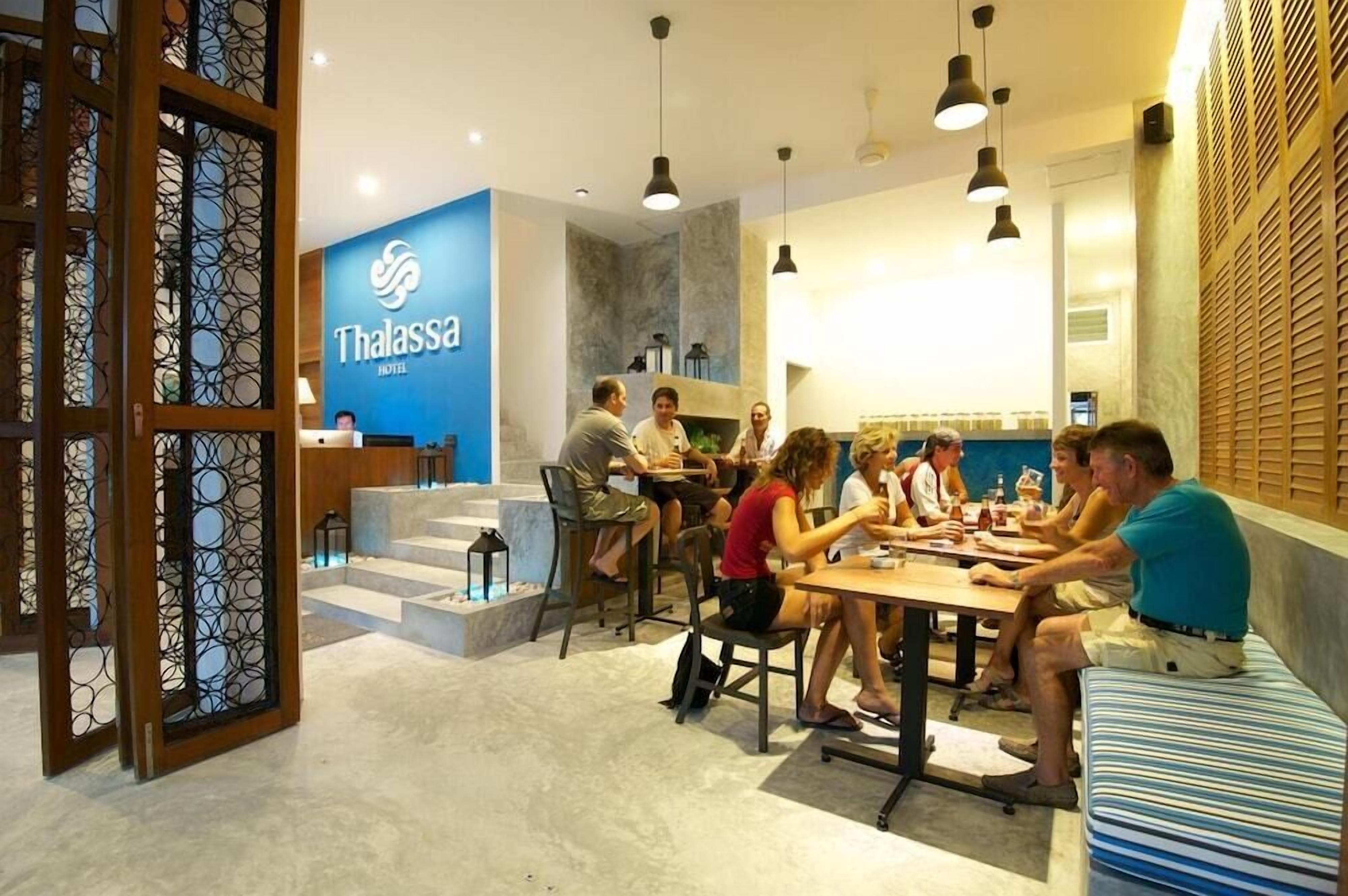 Un hall d'hôtel moderne avec un comptoir d'accueil, des espaces de détente et une enseigne bien visible indiquant « Thalassa Hotel ».