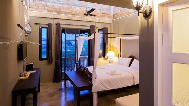 Una habitación de hotel con cama, escritorio, silla, balcón con cortinas y ventilador de techo.