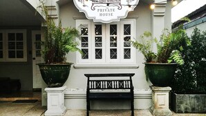 Una casa particular con un letrero, un banco y plantas en macetas.