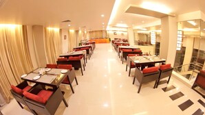 A hotel dining area with multiple tables and chairs, a central stage, and a staircase.
