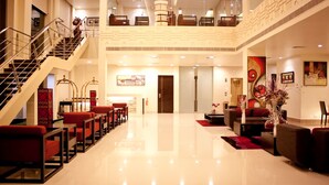 A spacious lobby with a high ceiling, a staircase, and a seating area with red and black furniture.