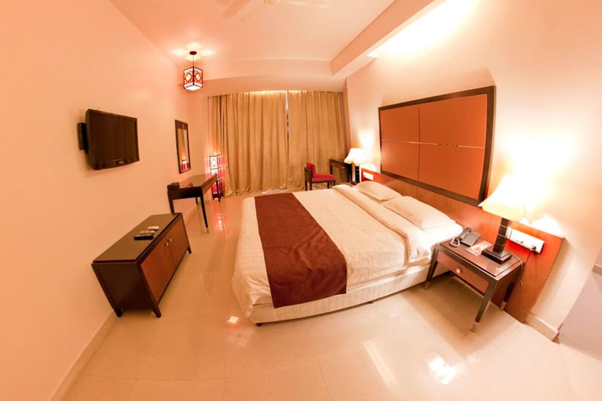 A hotel room with a large bed, a desk, a chair, a television, and a wardrobe.