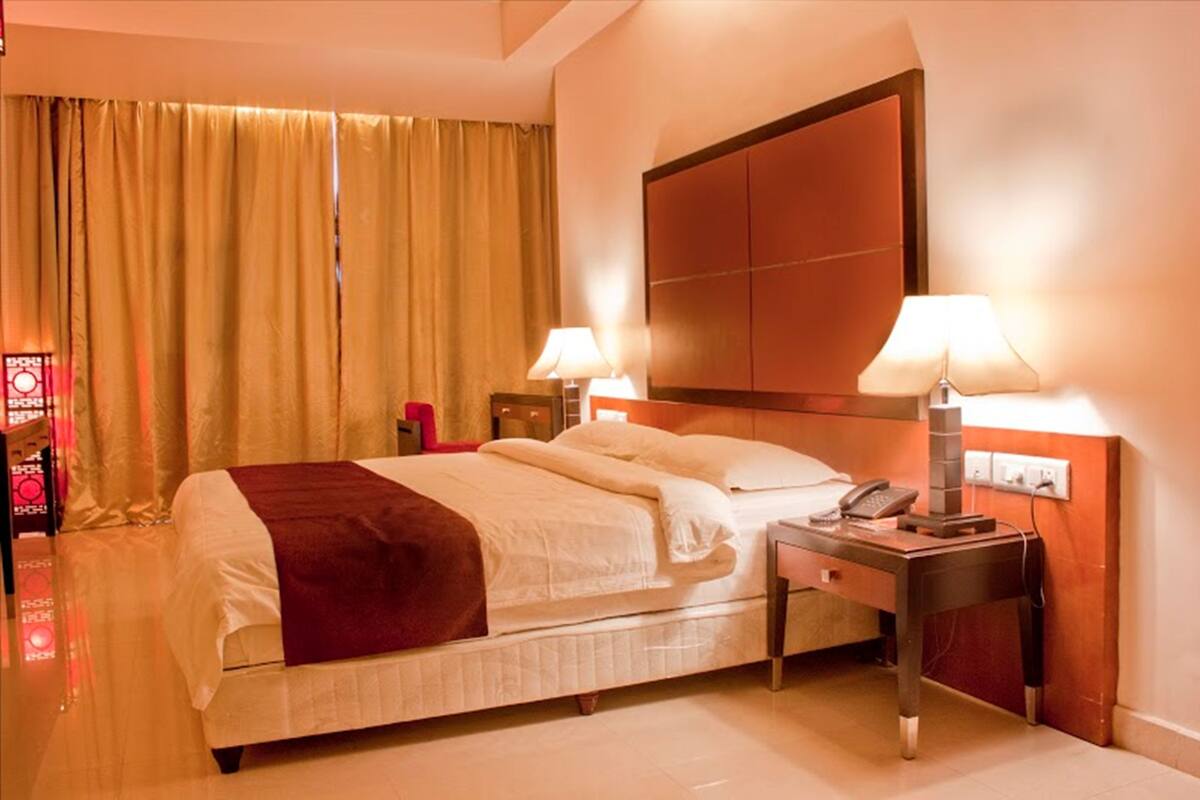 A hotel room with a large bed, two bedside tables with lamps, a wooden headboard, and a curtain on the window.
