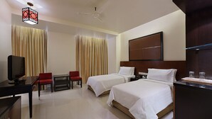 A hotel room with two beds, a desk with a television, a chair, and a ceiling fan.