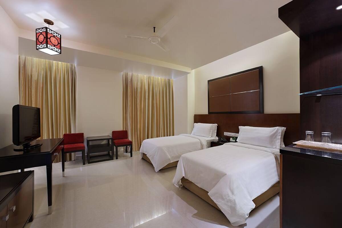 A hotel room with two beds, a desk with a television, a chair, and a ceiling fan.
