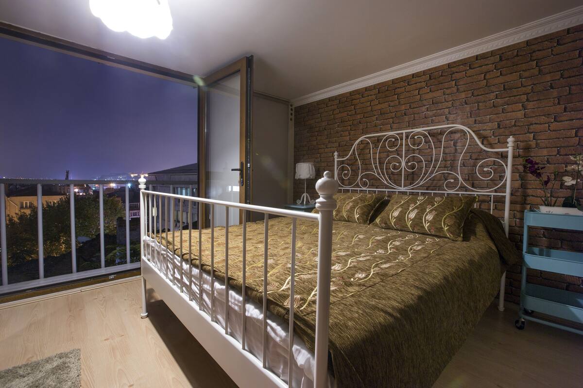 A bedroom with a metal bed frame, a brick wall, and a view through a balcony door.