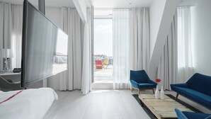 Een hotelkamer met een bed, een televisie, een blauwe bank, een stoel en een groot raam met gordijnen.