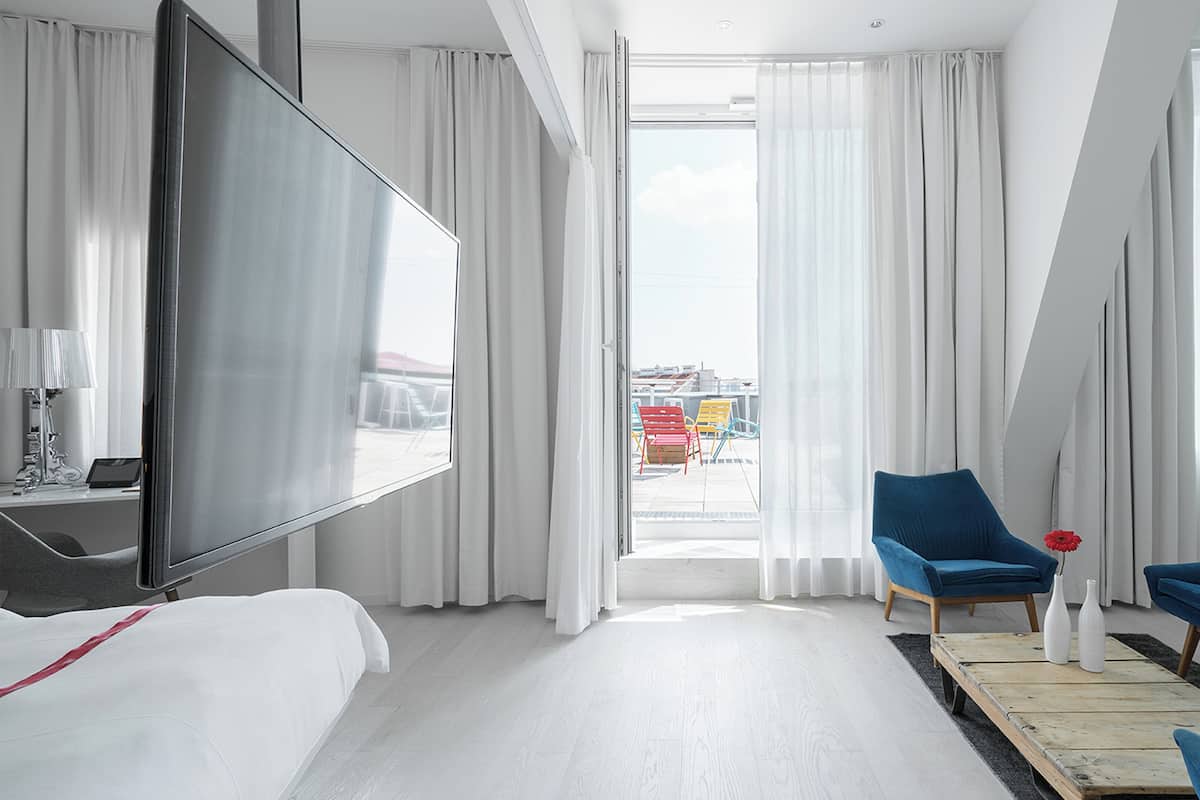 A hotel room with a bed, a TV, a blue sofa, a chair, and a large window with curtains.