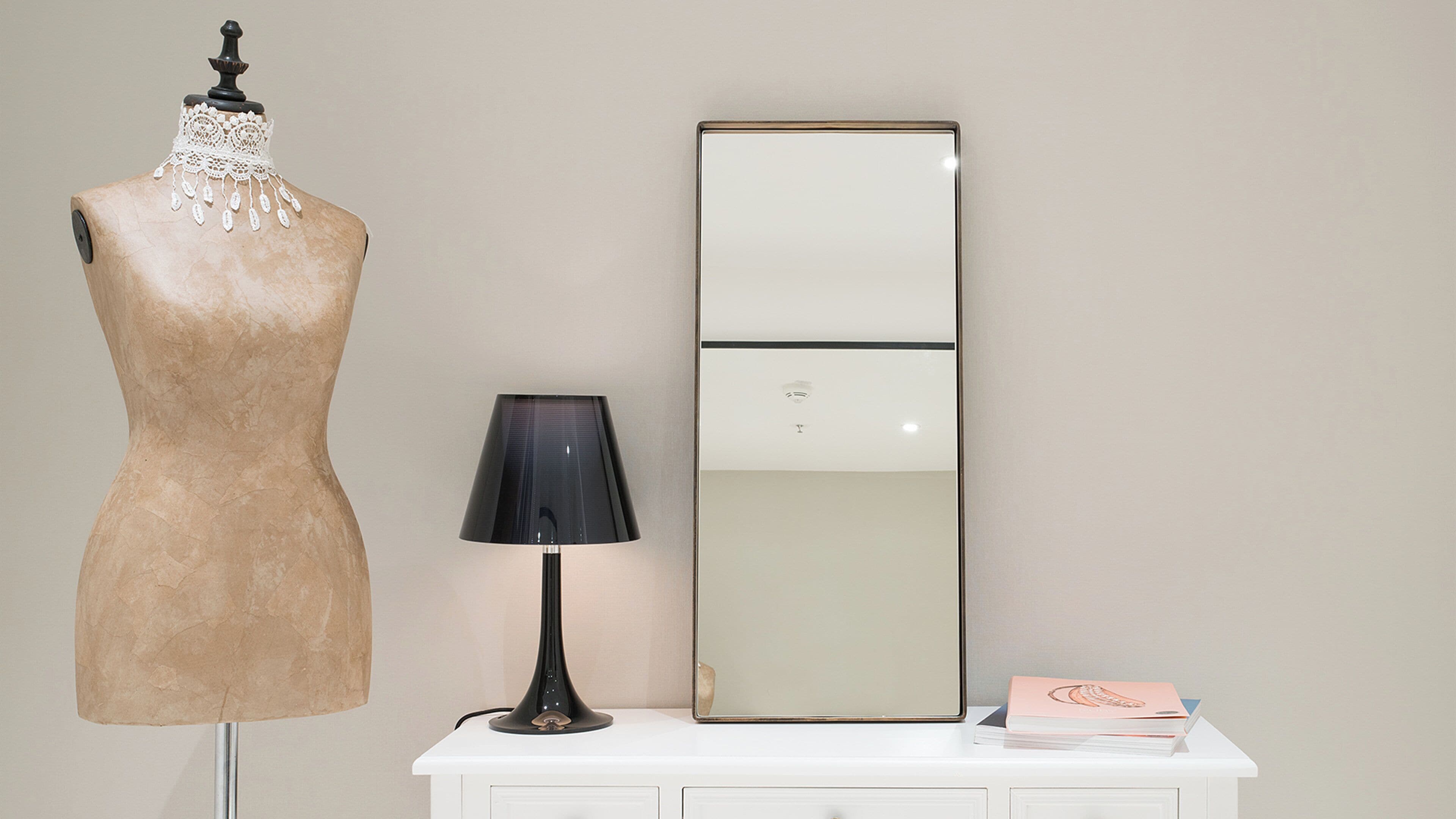 A mannequin, a lamp, a mirror, and a white dresser.