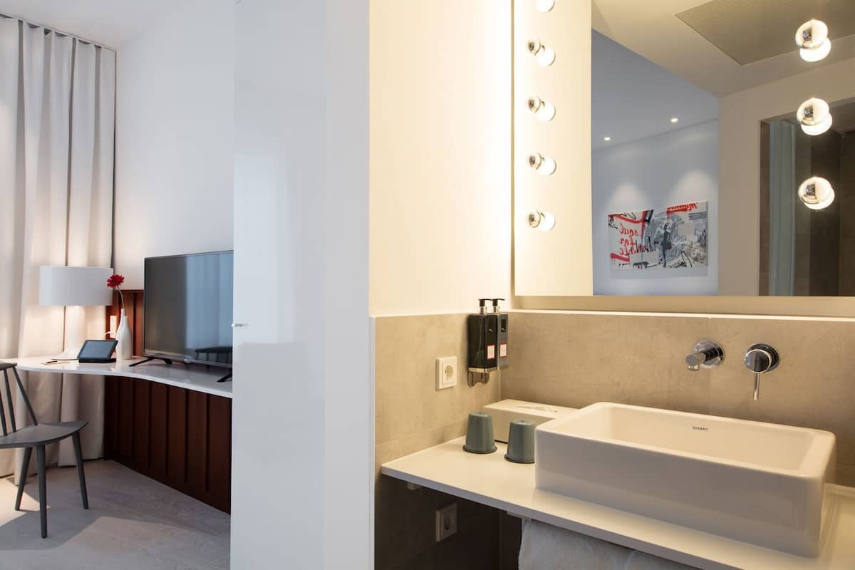 A modern hotel room with a large bathroom, a desk with a laptop, a chair, and a television.
