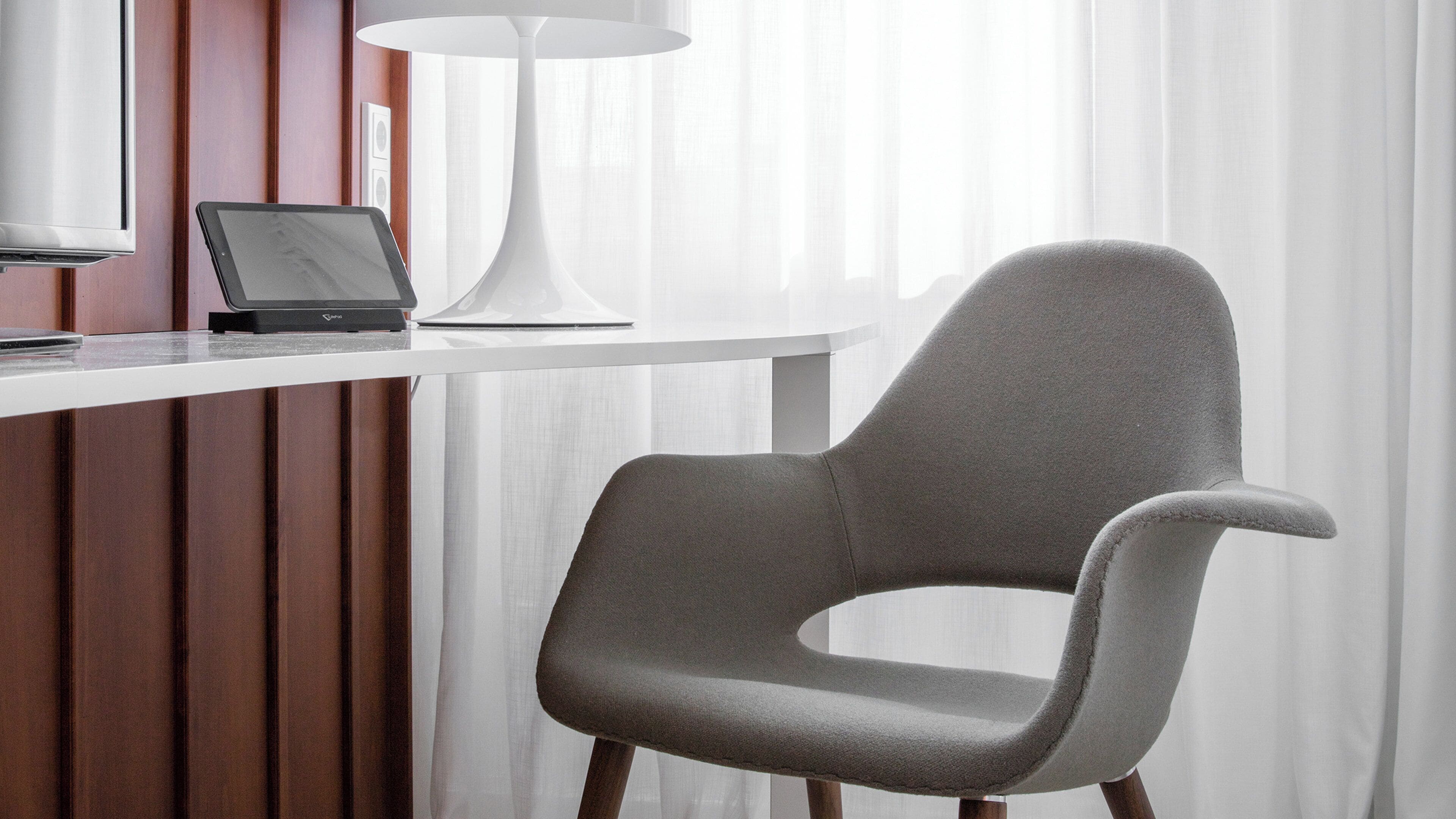 A modern office chair with a high backrest and armrests, positioned next to a white desk with a laptop and a white lamp.